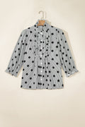 A Women's blac and white Striped Polka Dot Ruffle Neck Shift Blouse , featuring a ruffled front placket and button-down design, hanging on a wooden hanger against a beige wall. 