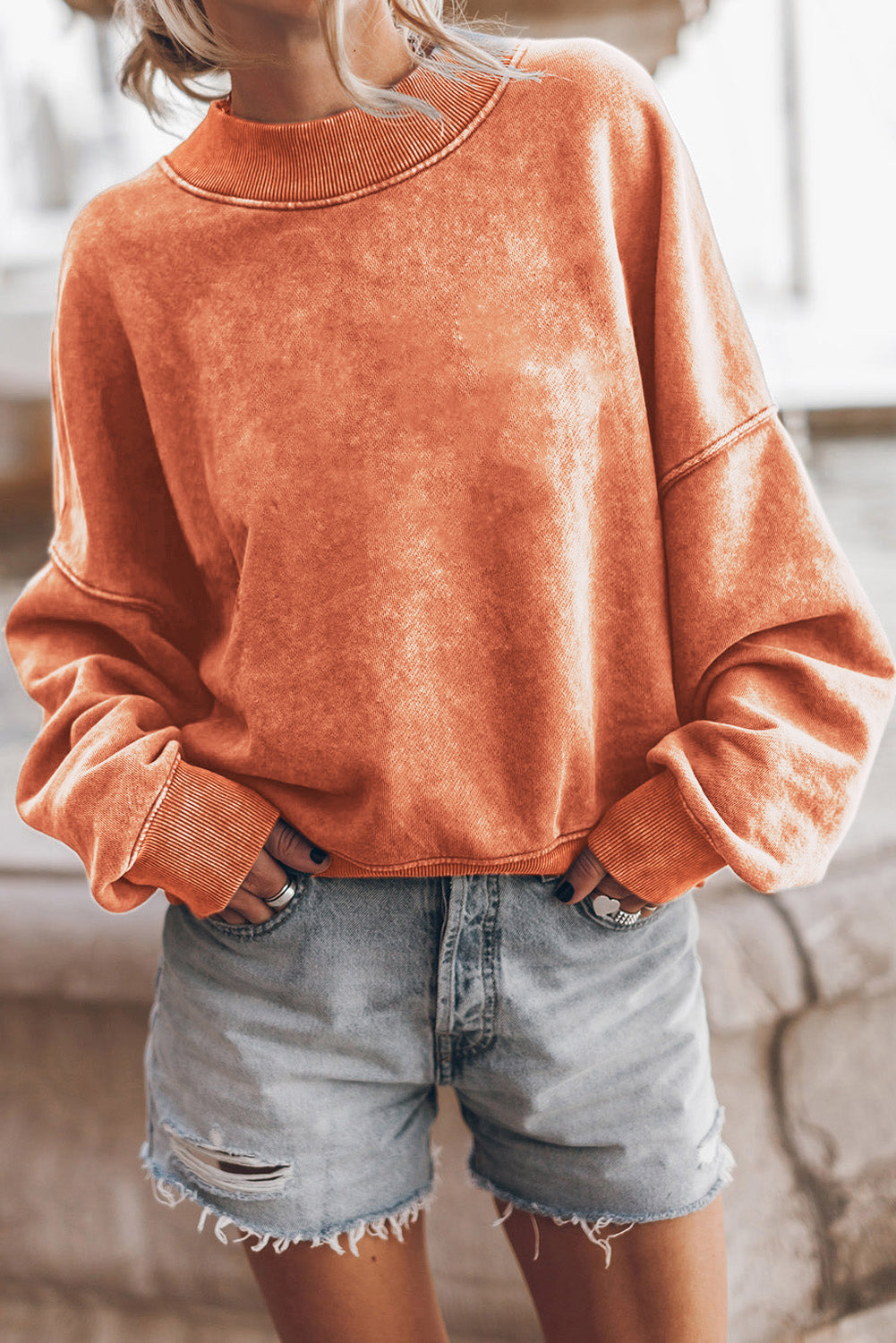 Person wearing an orange sweatshirt and denim shorts indoors