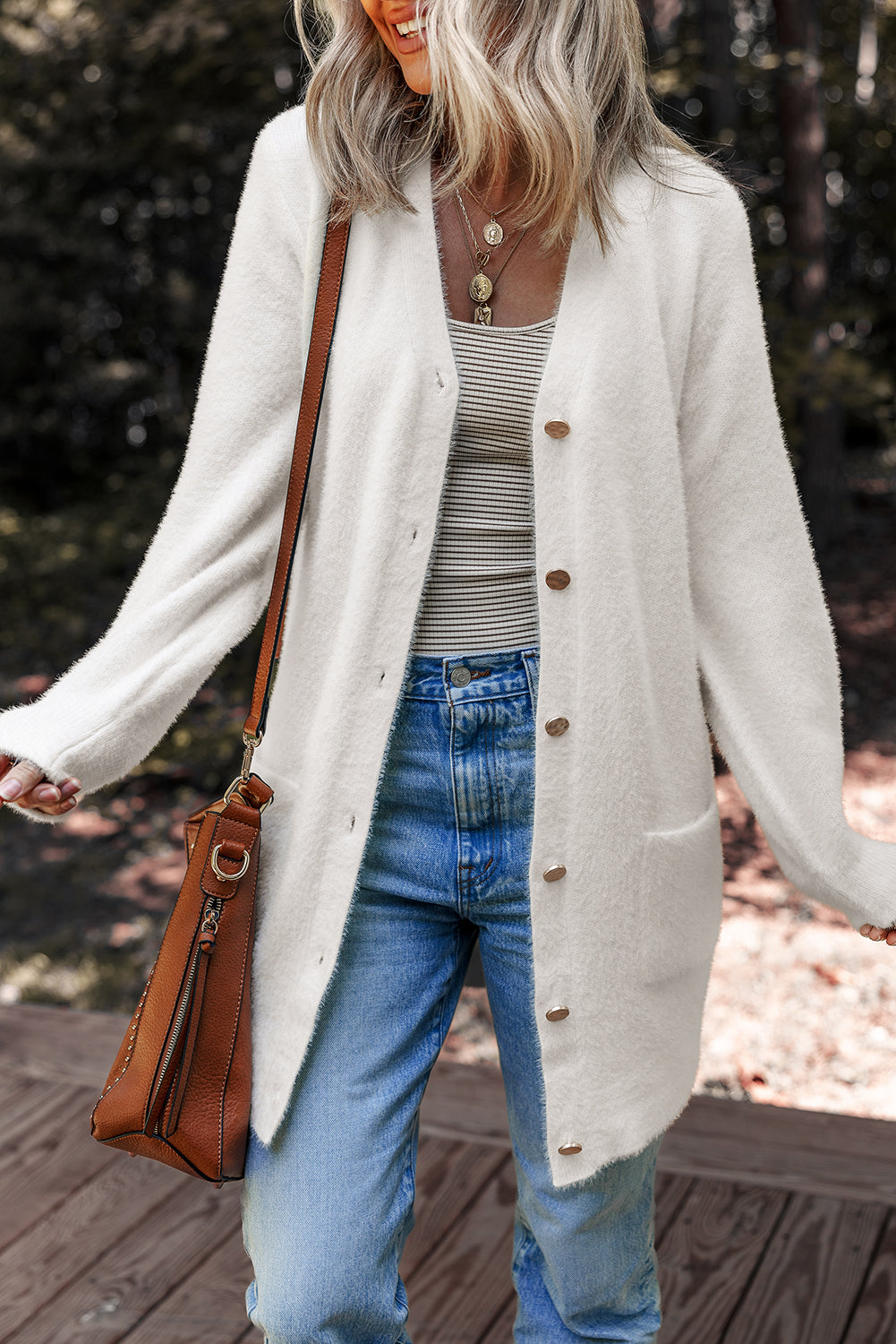 Person wearing a long white Fuzzy Buttoned Midi Cardigan, striped top, and jeans, holding a brown leather bag.
