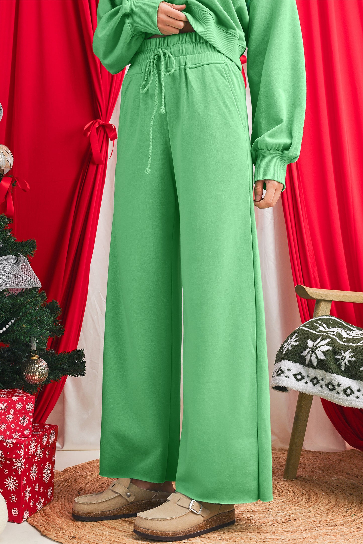 Person wearing a green outfit with wide-leg pants in a festive setting with red curtains and Christmas decorations.