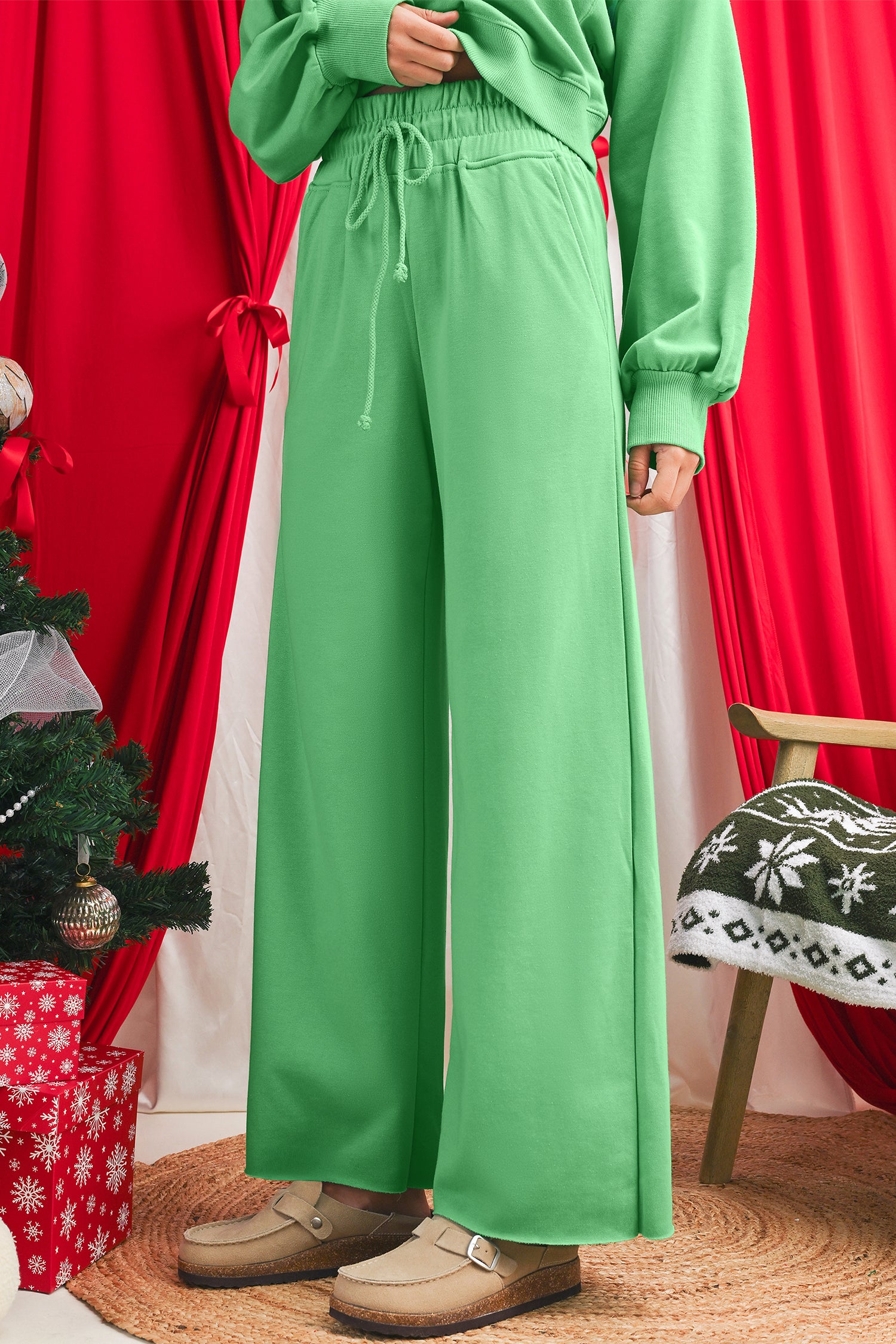 Person wearing a green outfit with wide-leg pants in a festive setting with red curtains and Christmas decorations.