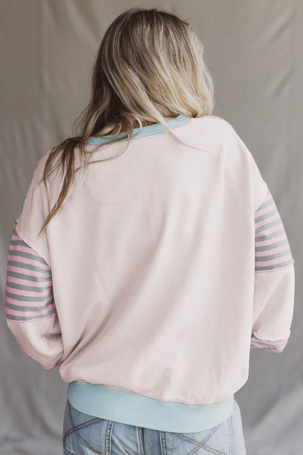 Person wearing a light pink sweater with striped sleeves against a plain background