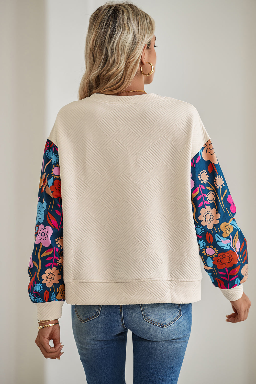 Woman wearing a cream sweater with floral sleeves against a plain background