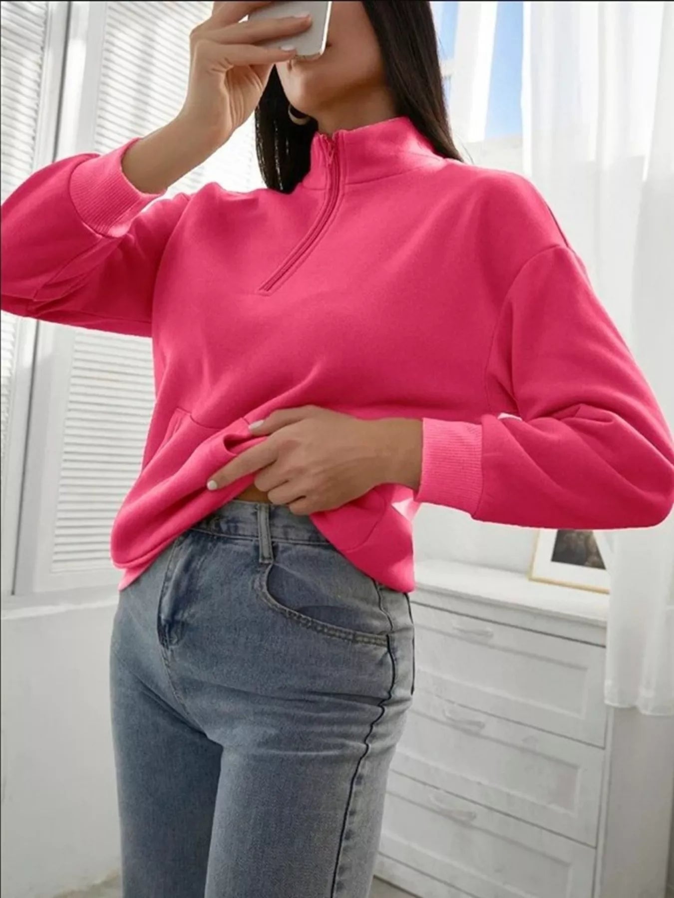 Person wearing a bright pink long-sleeve top and blue jeans indoors.