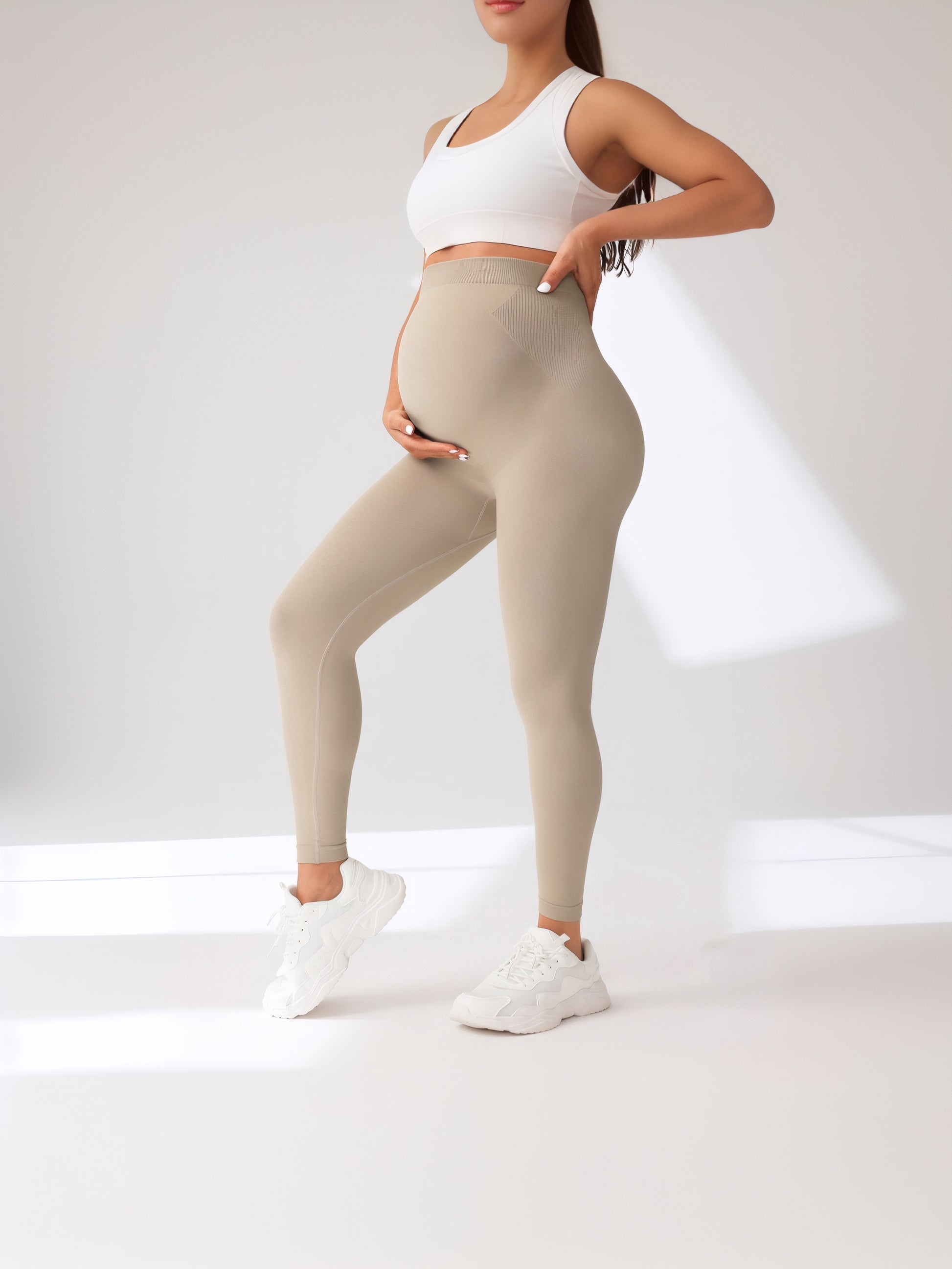Person wearing beige leggings and a white sports bra on a light gray background