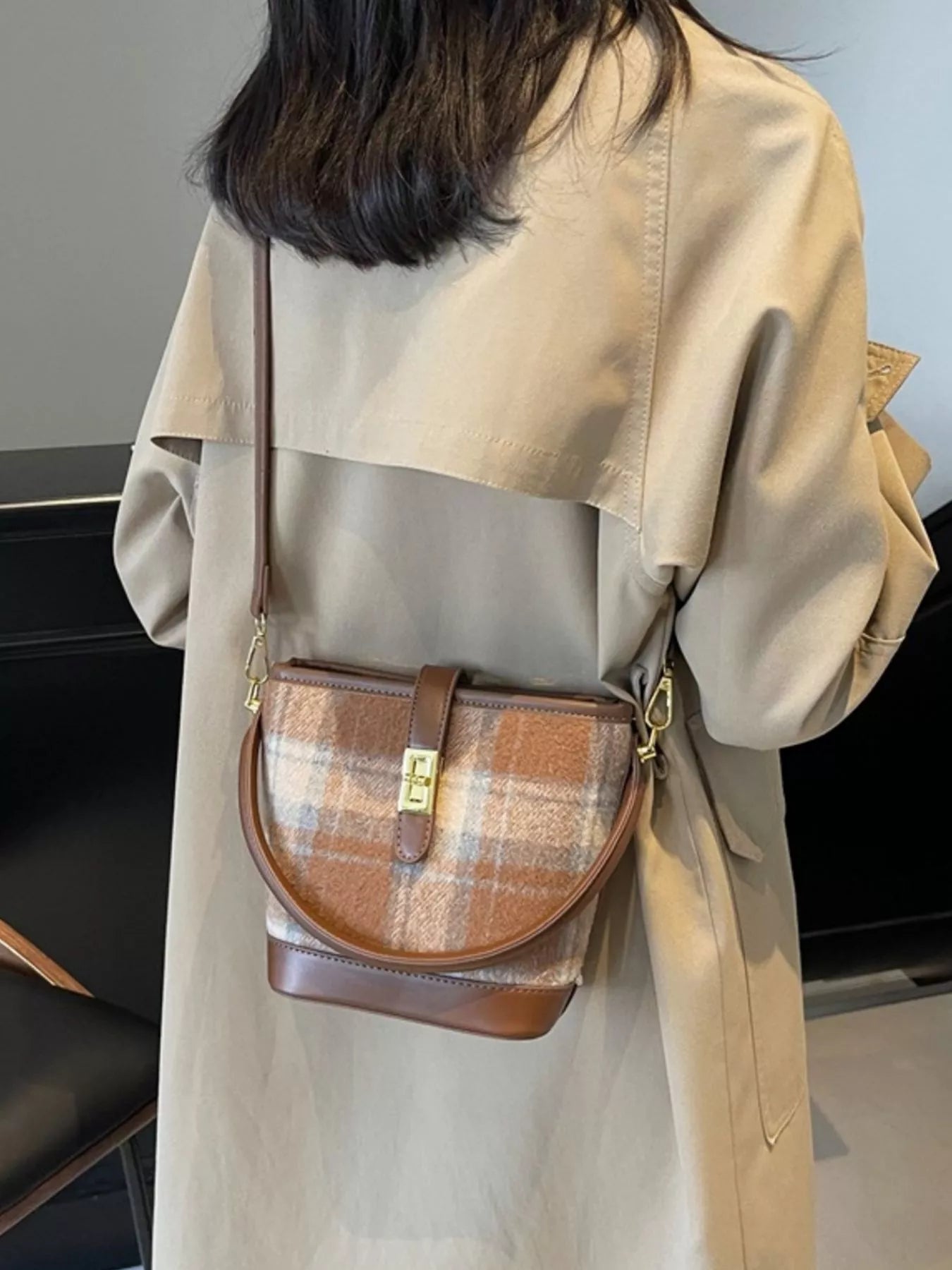 Person wearing a beige trench coat with a plaid patterned bag over one shoulder.