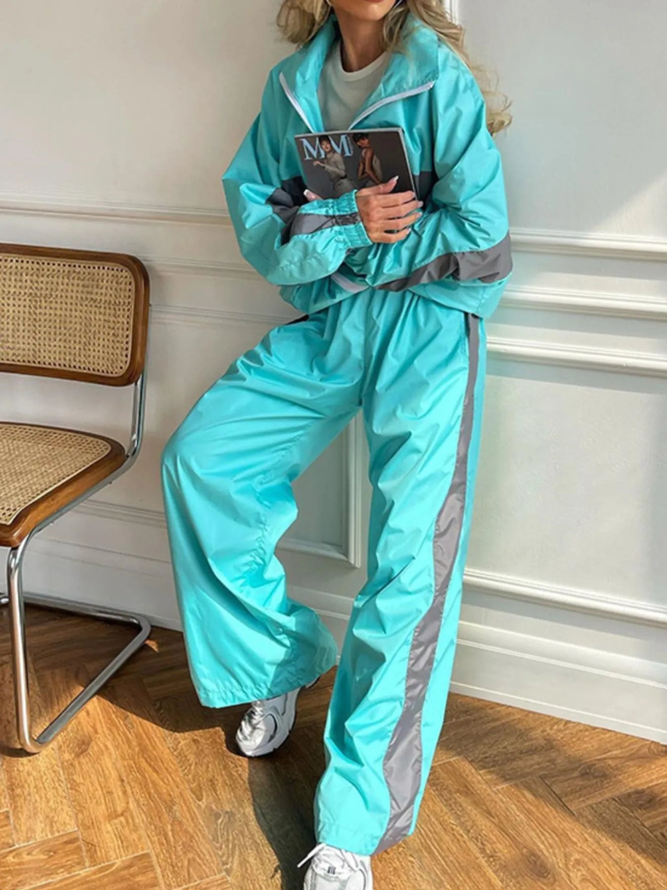 Person wearing a bright blue tracksuit with gray accents, holding a magazine indoors.