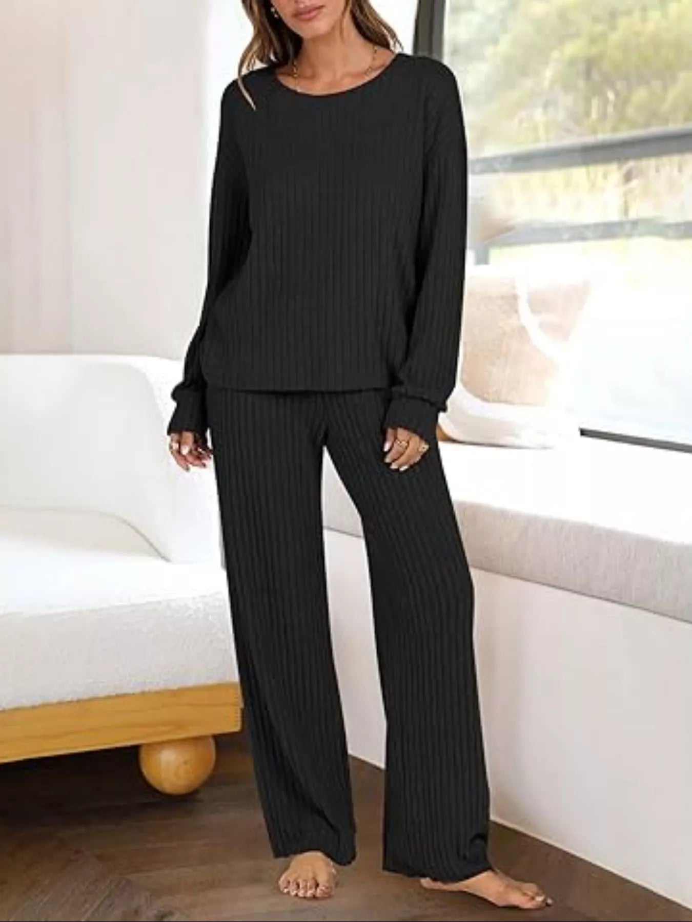 Person wearing a black ribbed lounge set in a home setting.
