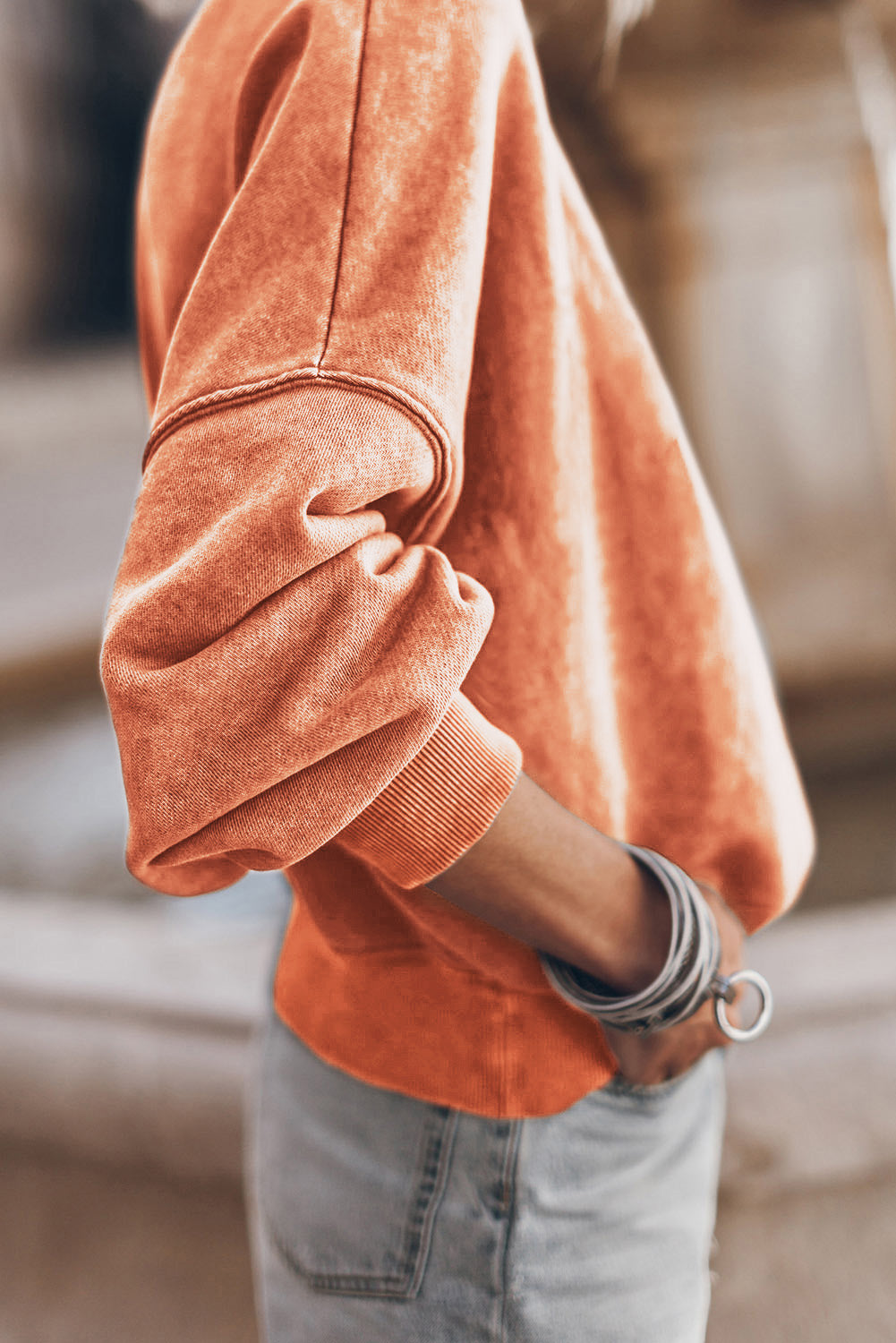 Close-up of an orange sweatshirt with rolled-up sleeves and a blurred background