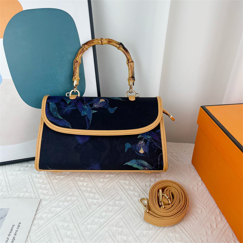Blue handbag with floral pattern and gold accents on a white surface