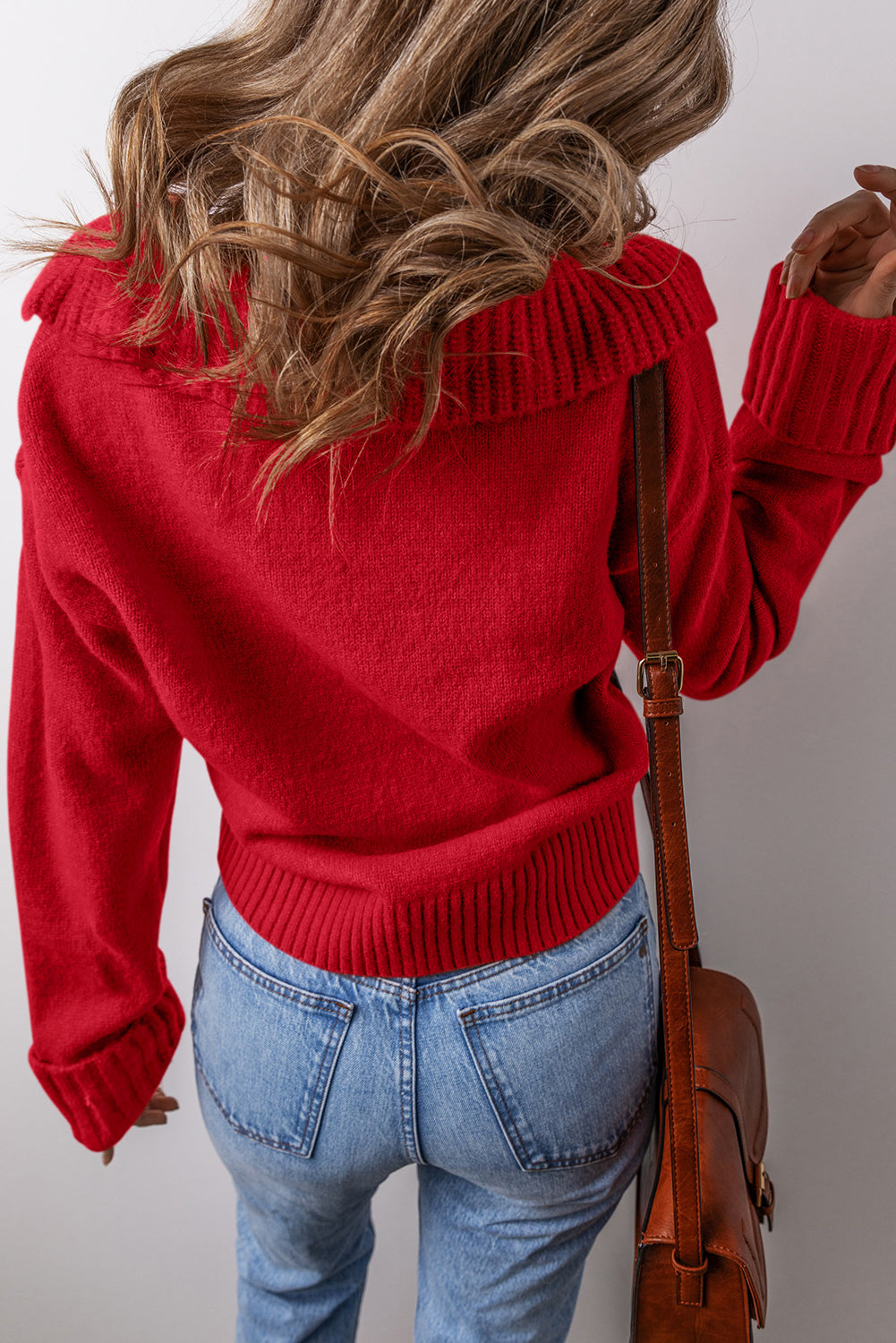 Person wearing a racing red Ribbed V-Neck Sweater  and blue jeans with a brown bag.