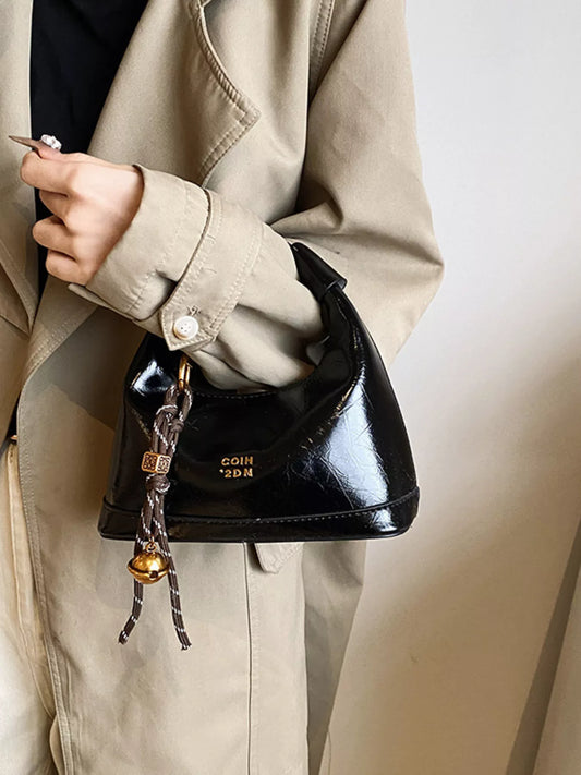 Person holding a black handbag with a decorative strap against a neutral background