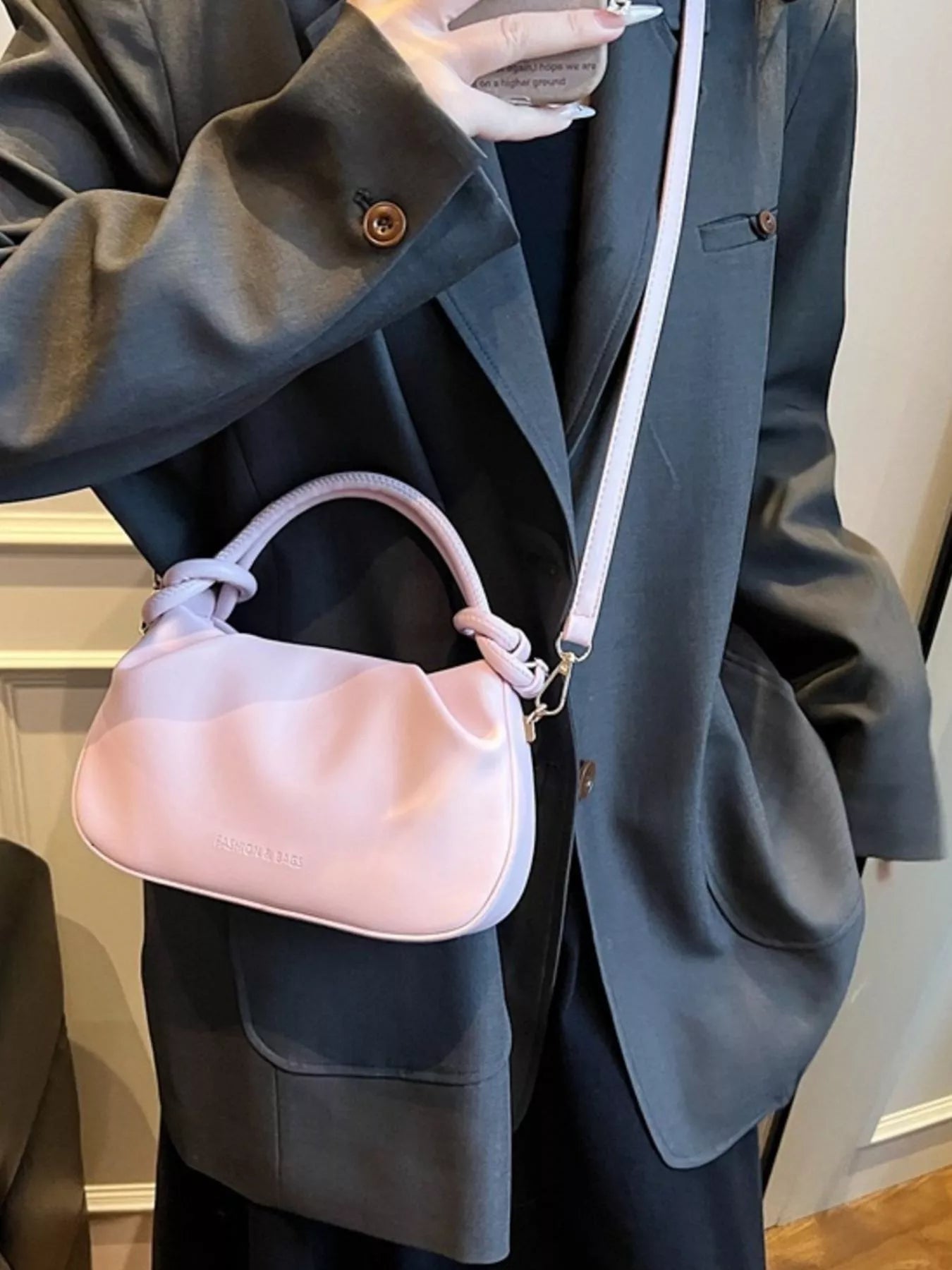 Person wearing a dark gray blazer holding a pink handbag.