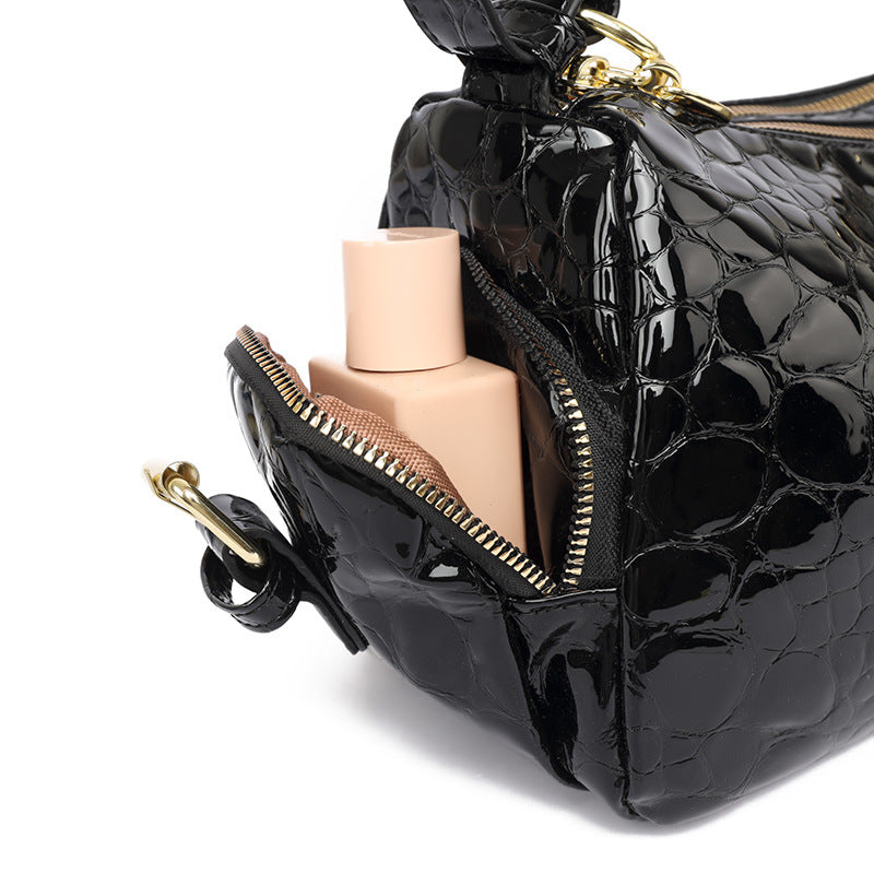 Black crocodile-patterned handbag with makeup products inside on a white background