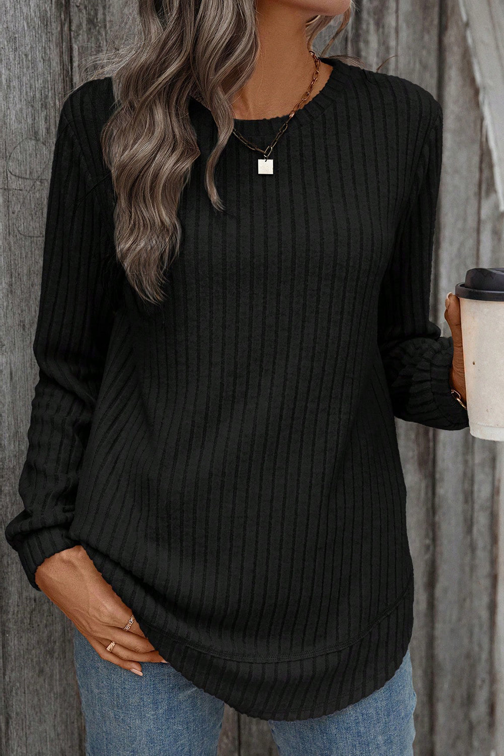 Person wearing a black ribbed sweater holding a coffee cup against a wooden background