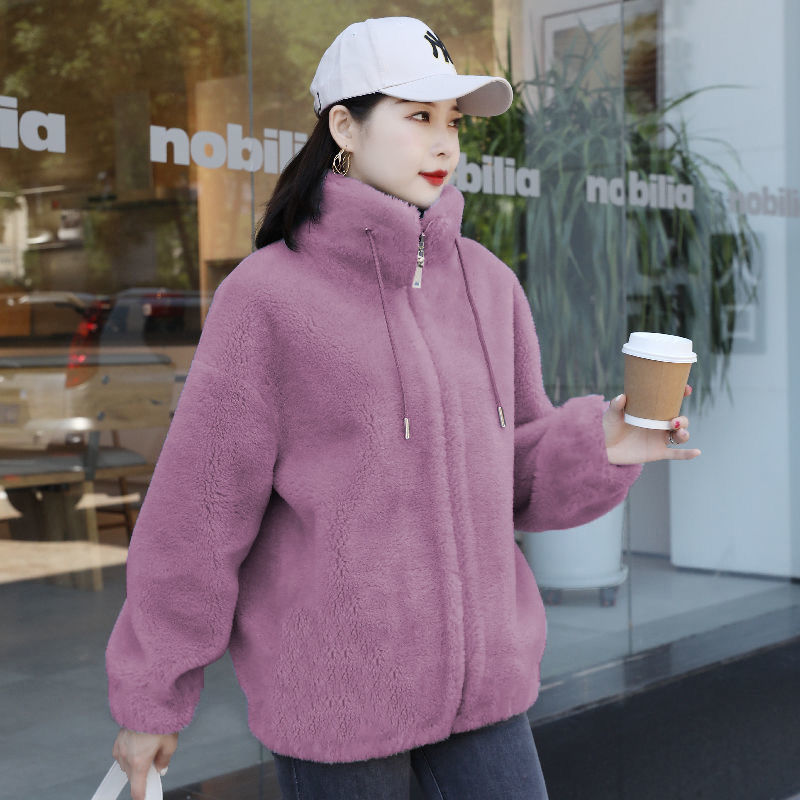 Woman in a purple fleece jacket holding a coffee cup in front of a store.