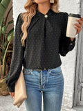 A woman wearing a black long sleeve blouse with a Swiss dot pattern and a mock neckline, paired with blue jeans and holding a cup.