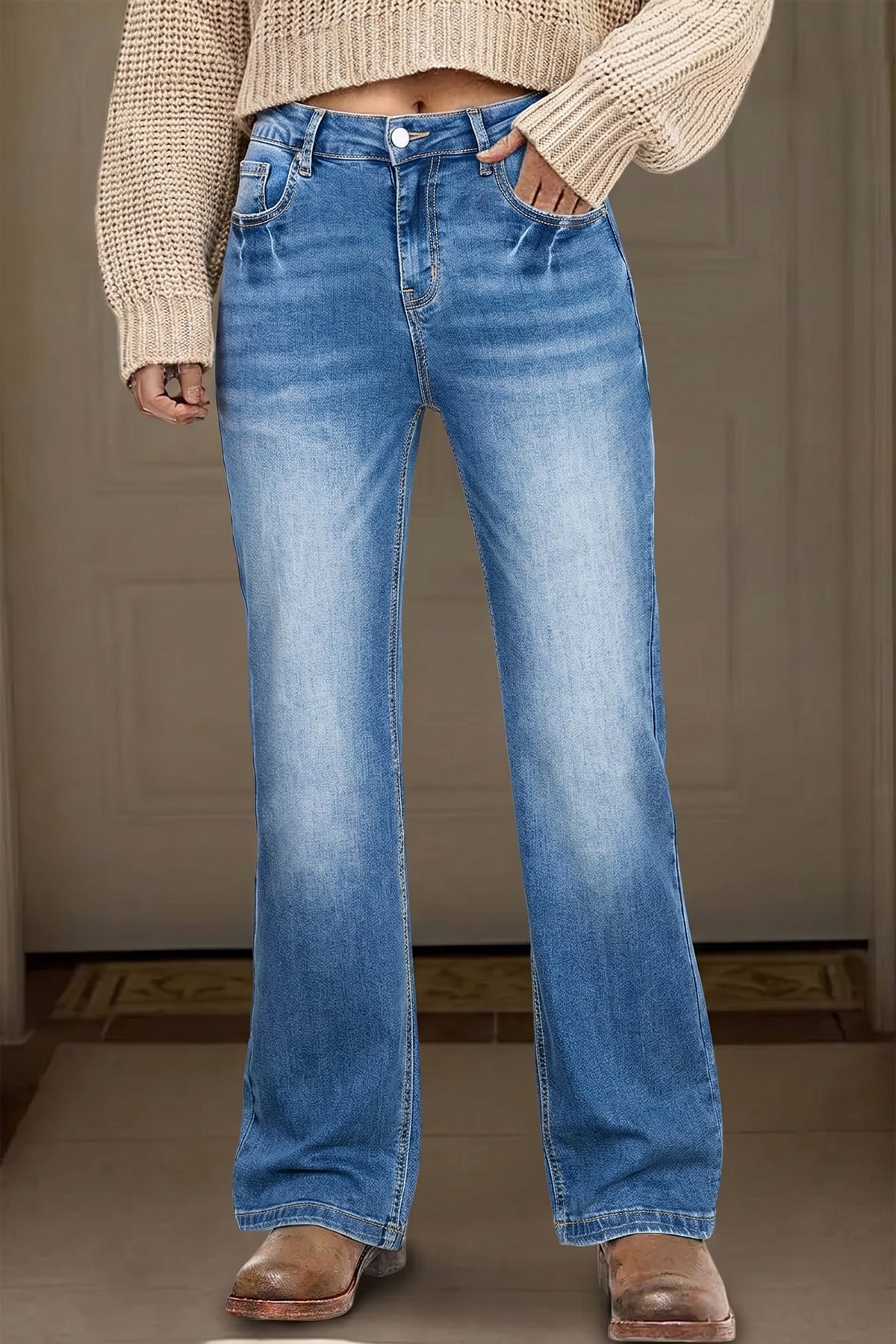 Person wearing blue jeans and a beige sweater against a neutral background