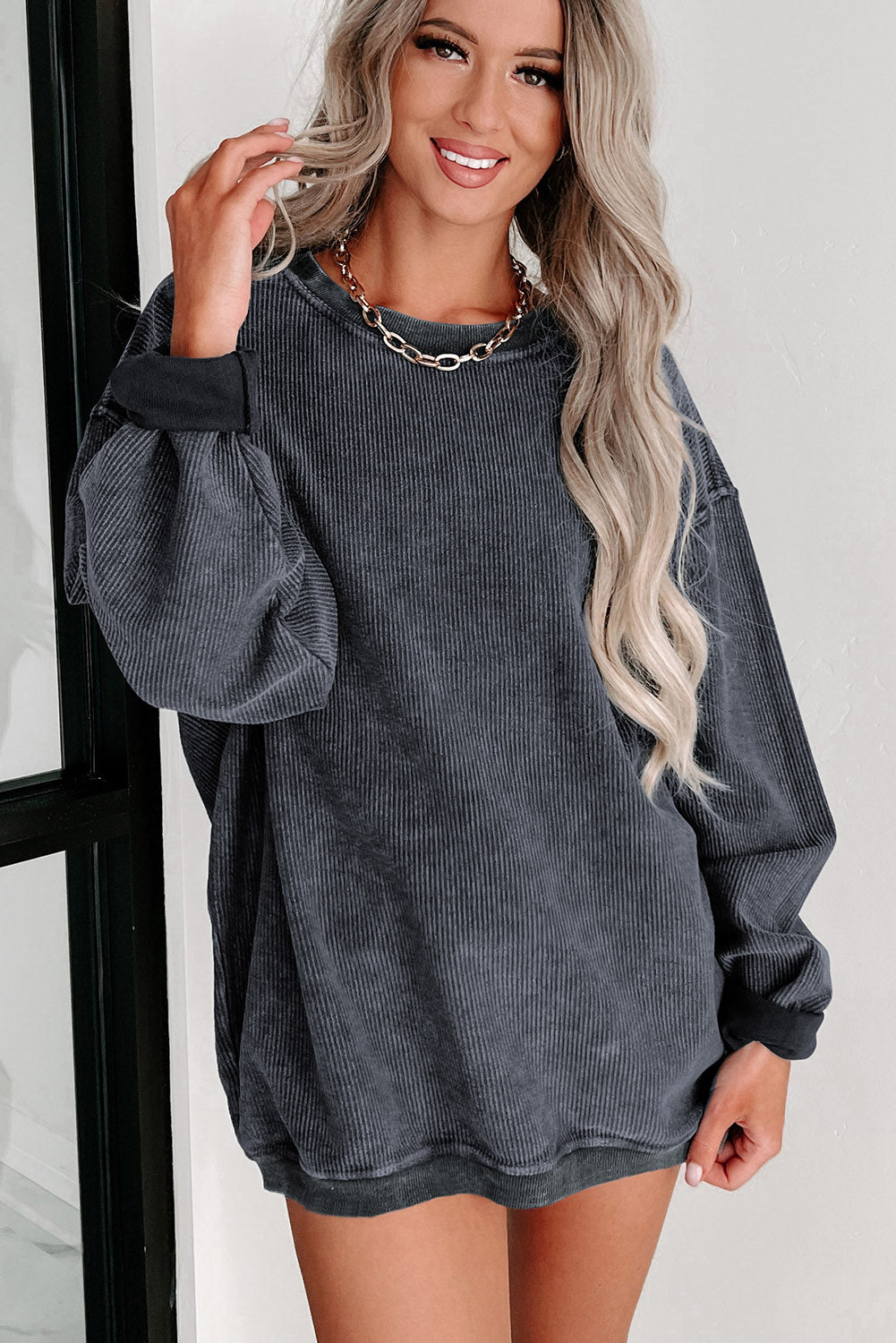 Model posing in a dark grey ribbed sweatshirt, emphasizing the soft texture and relaxed silhouette, with a confident smile.