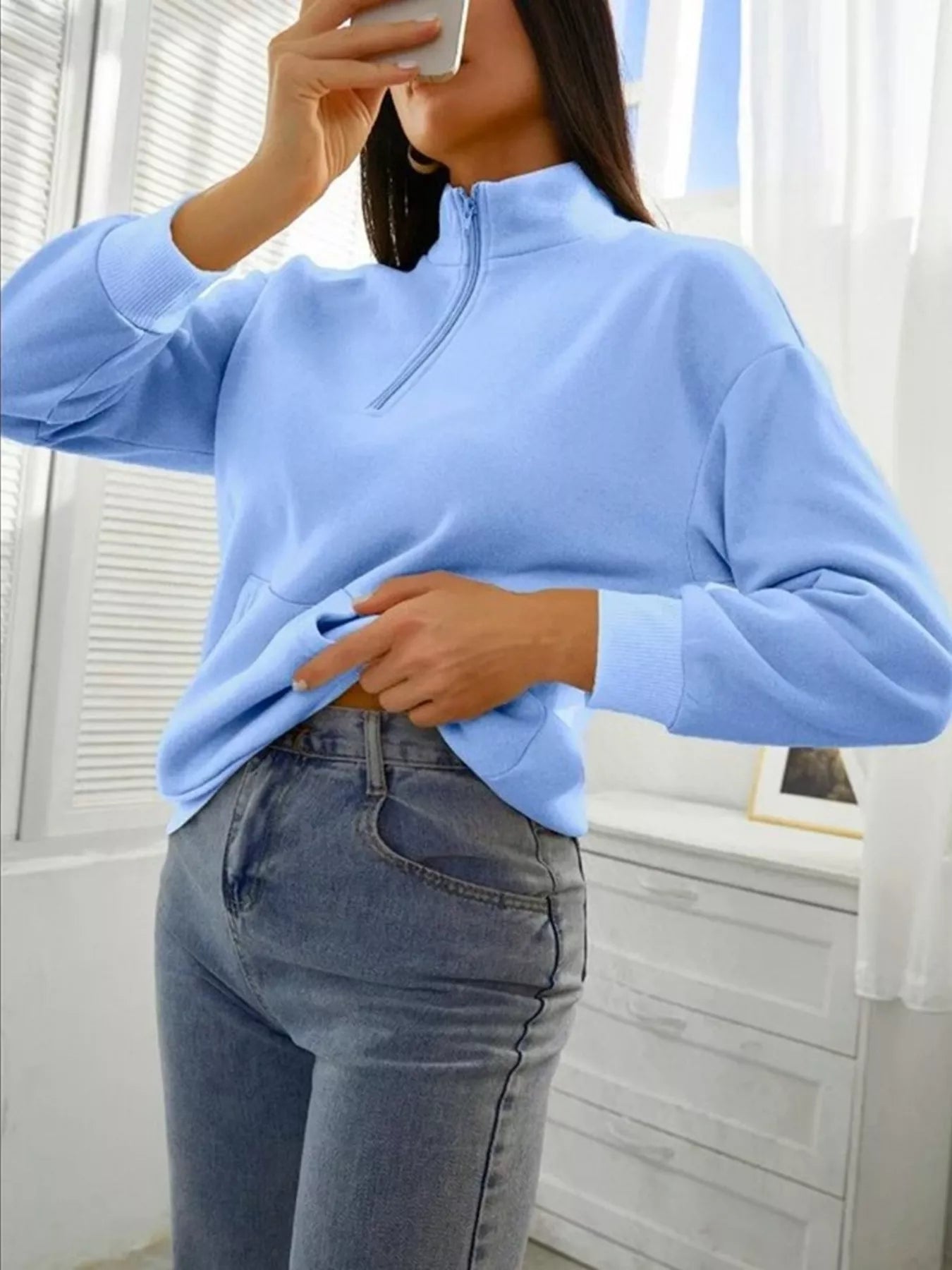 Person wearing a light blue sweater and jeans indoors.
