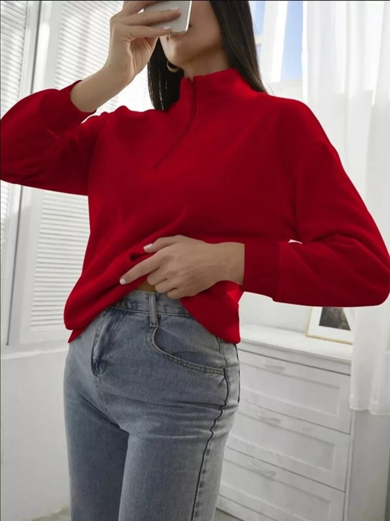 Person wearing a red sweater and blue jeans indoors.
