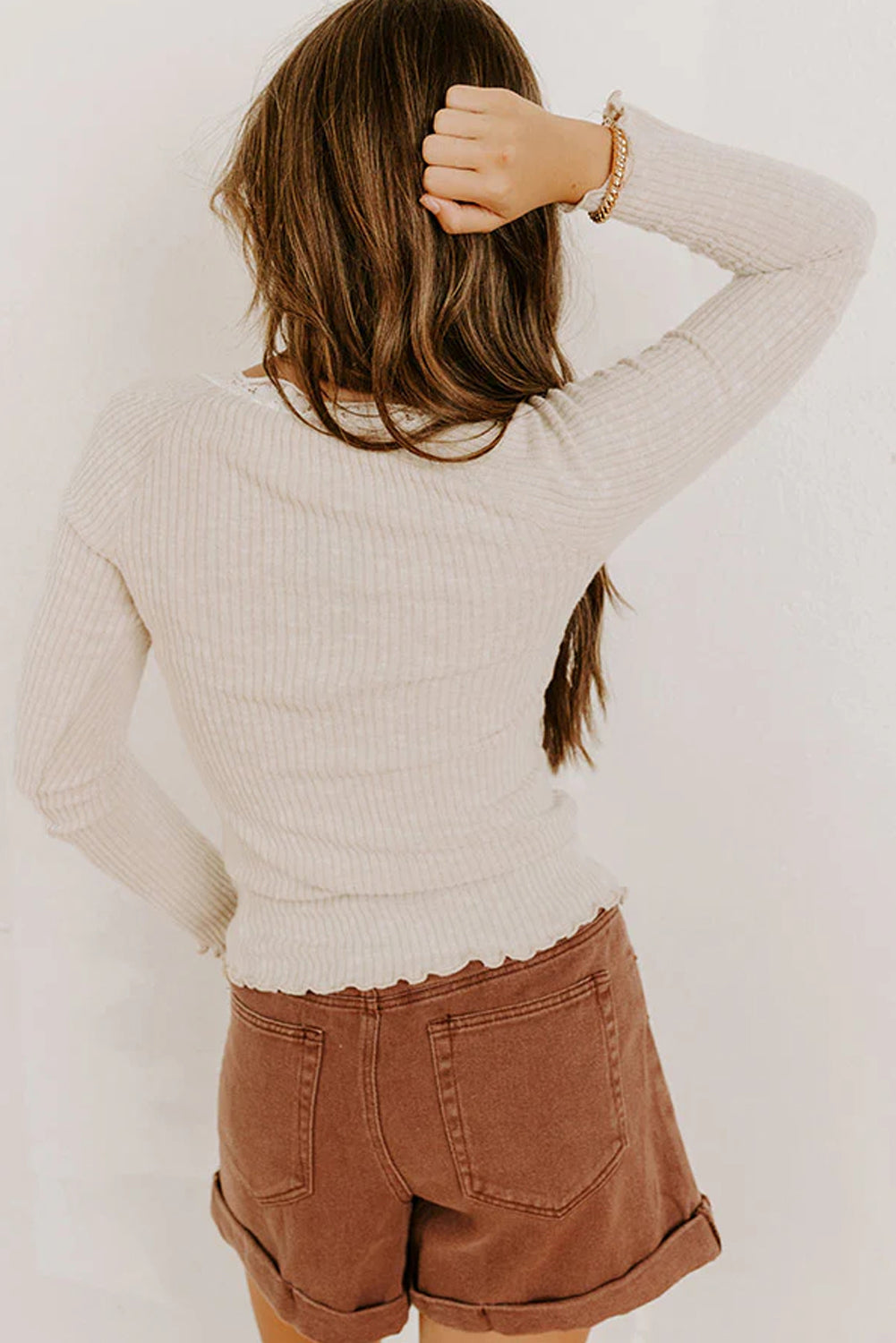 Person wearing a beige sweater and brown shorts against a white background