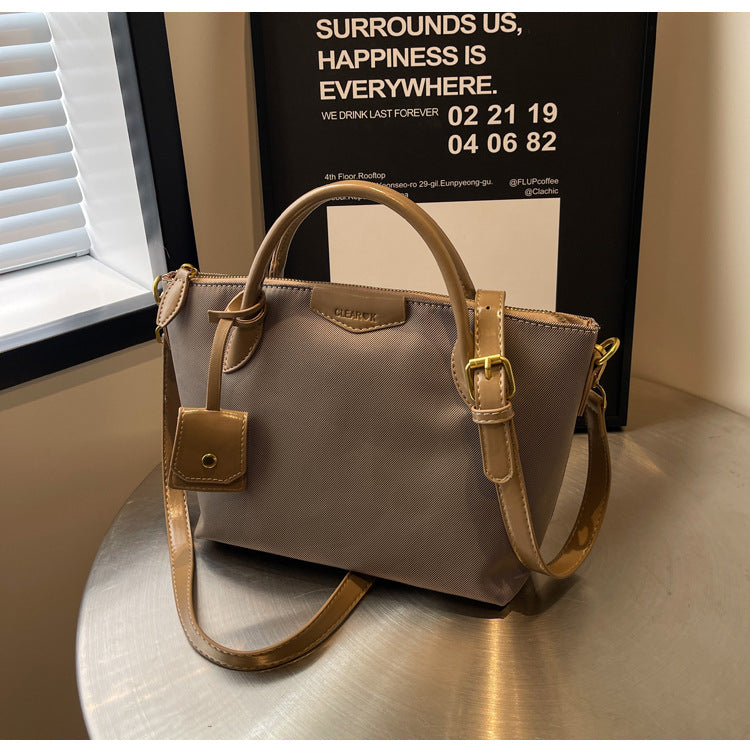 Beige handbag with brown strap on a metallic surface, with a blurred background.