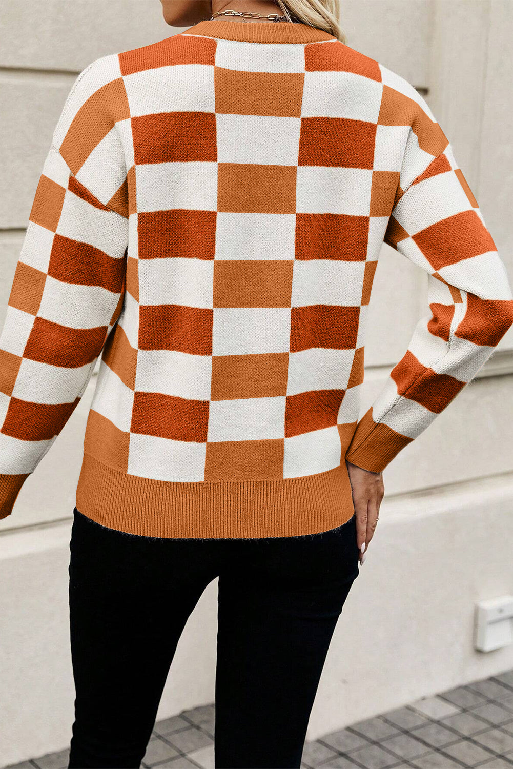 Person wearing a checkered sweater with orange and white squares, standing against a light-colored wall.