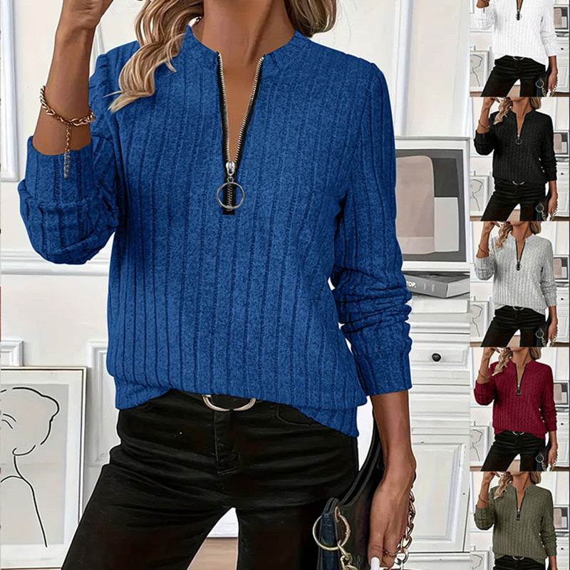 Woman wearing a blue ribbed sweater with a zipper, standing in a room with white walls and decor.