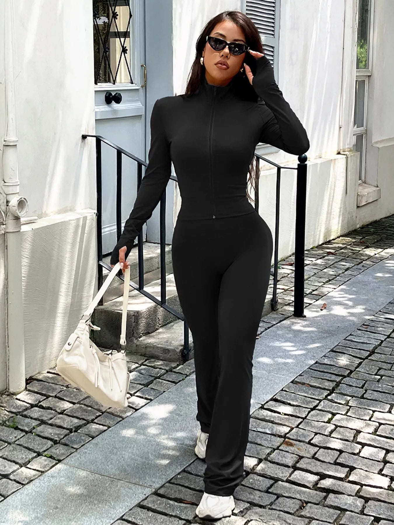 Woman in a black outfit standing on a sidewalk with a white building in the background