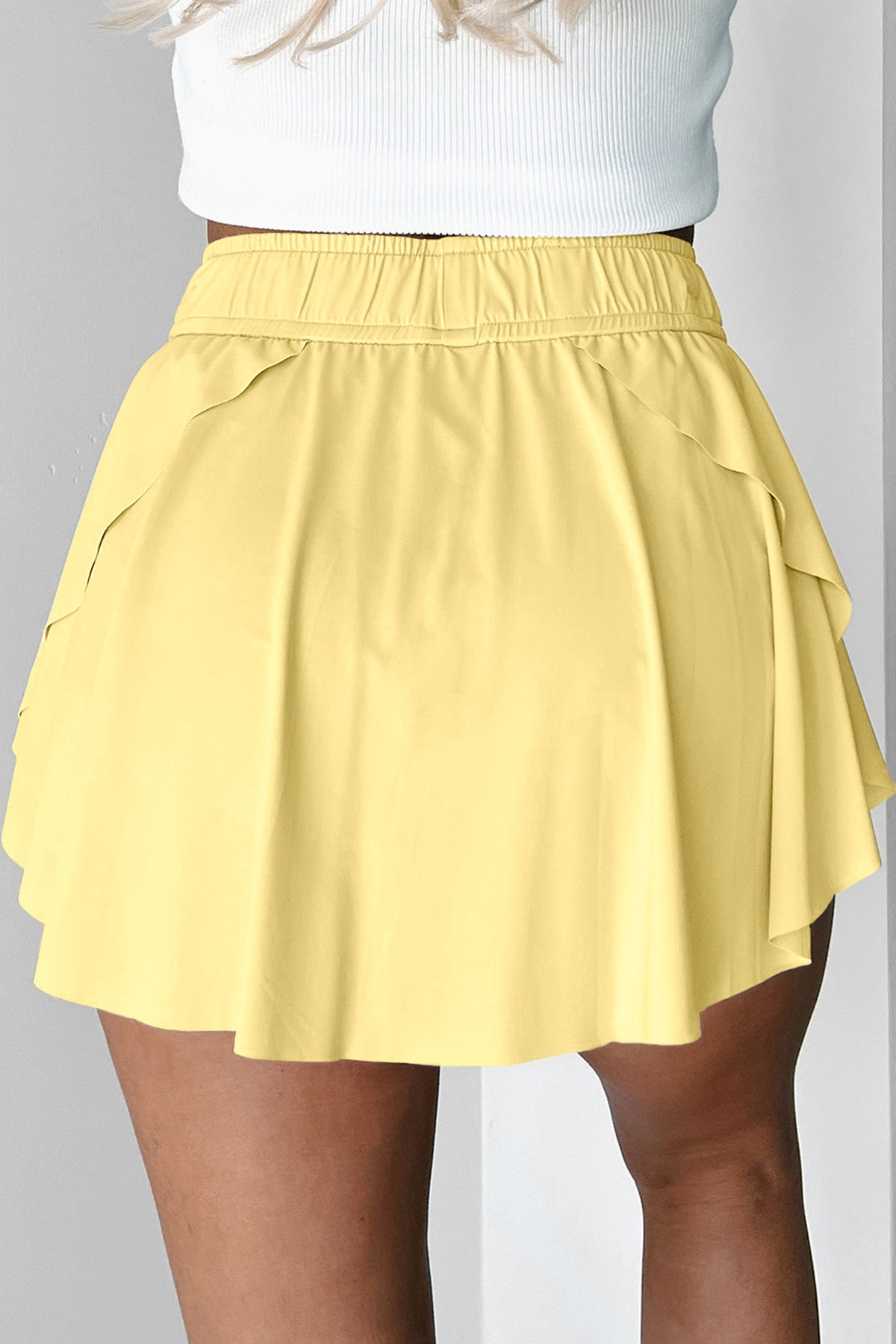 Yellow tennis skort worn with a white top on a gray background back view