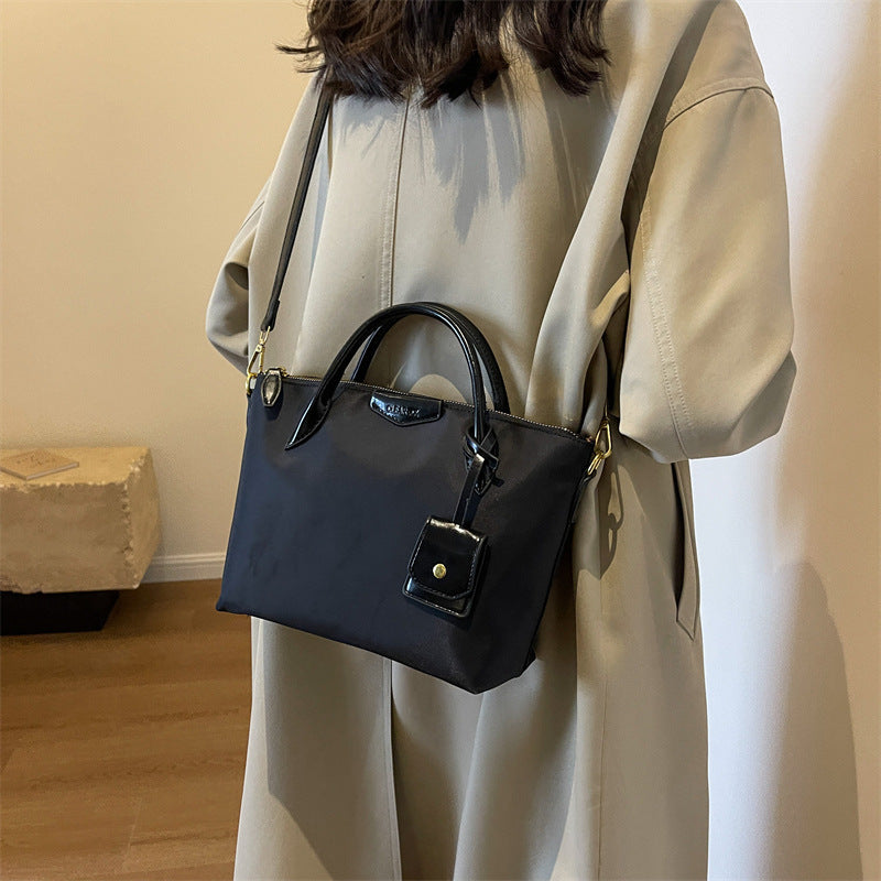 Person wearing a beige coat holding a black handbag indoors.