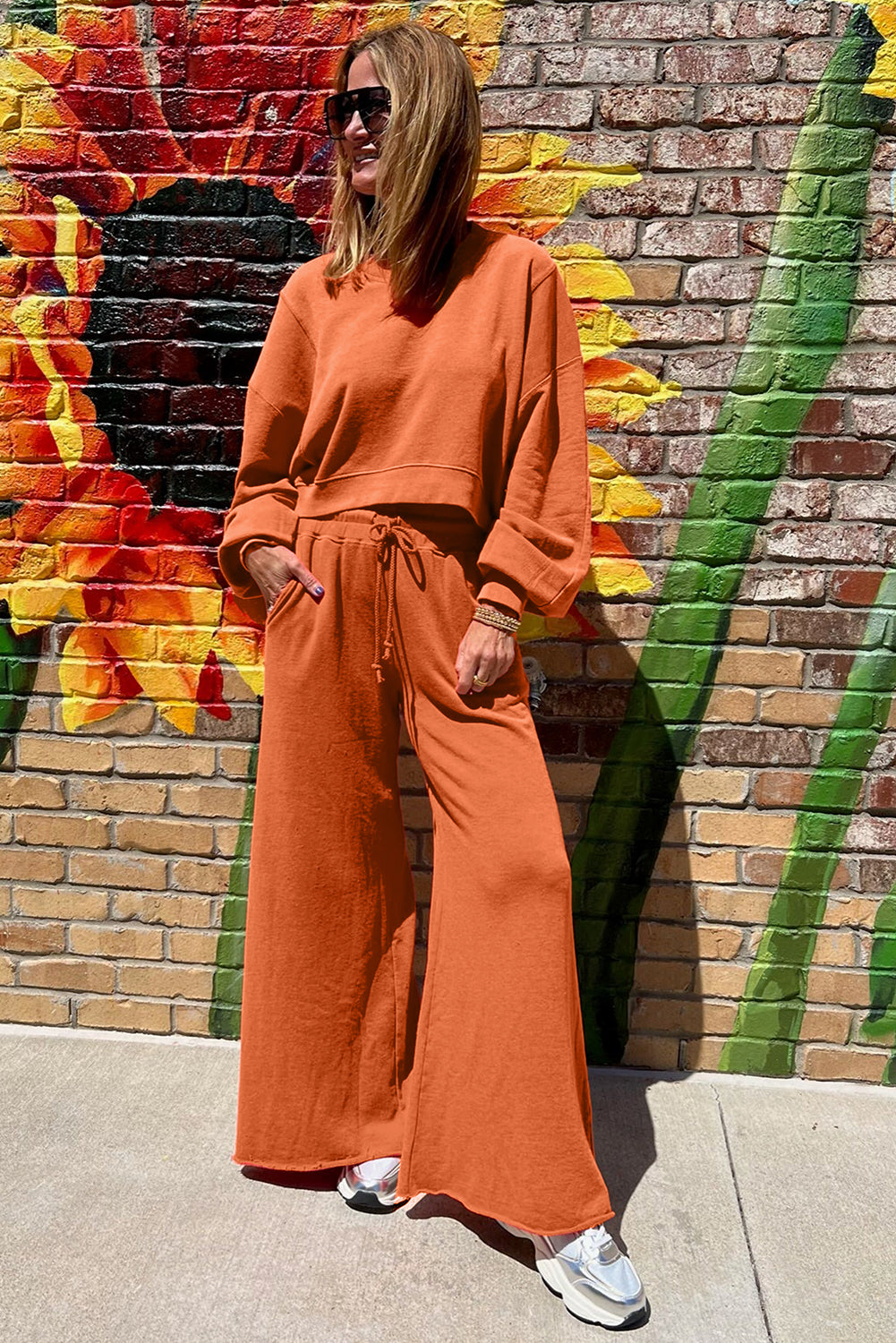 Person wearing an orange outfit standing in front of a colorful mural on a brick wall.