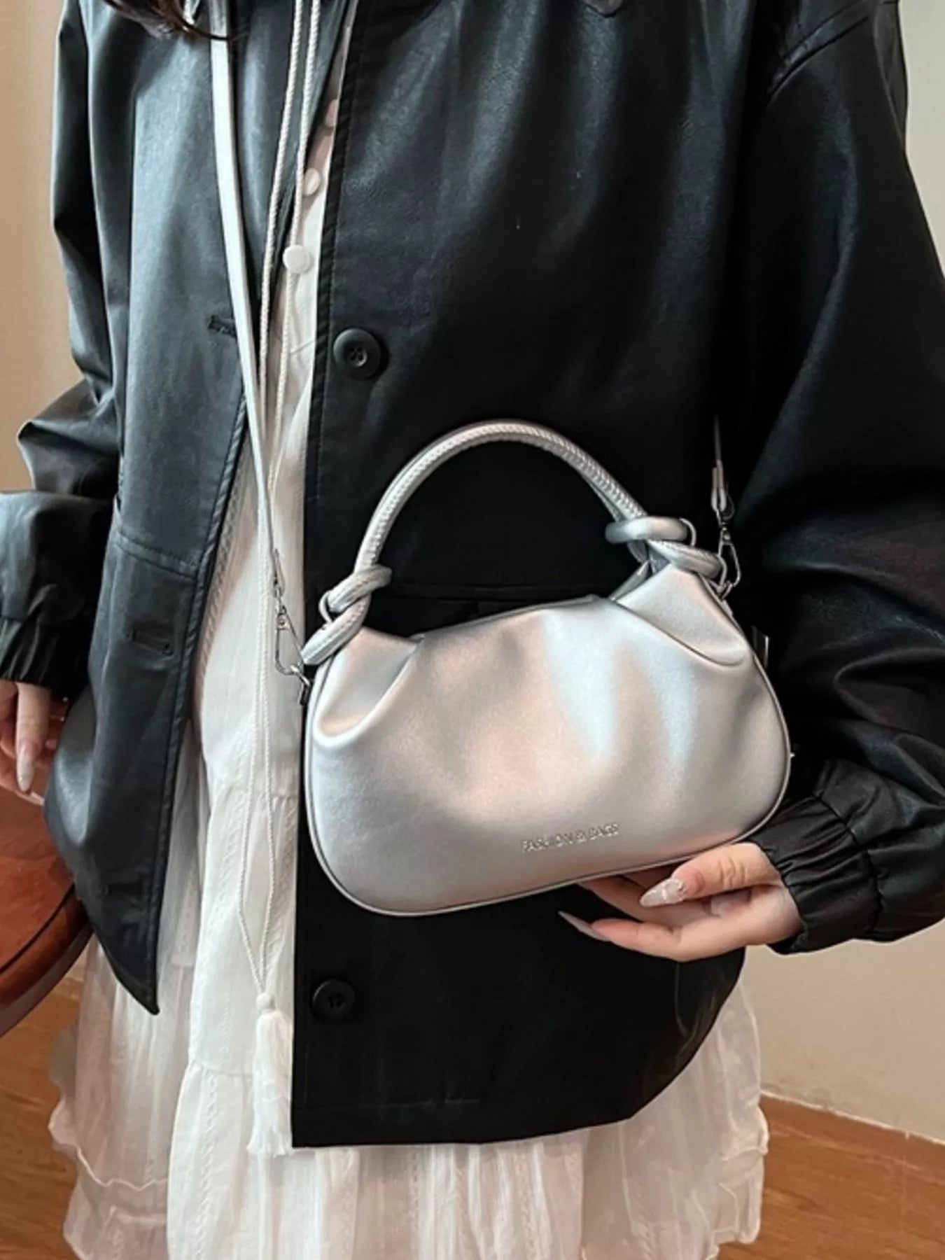 Person holding a silver handbag with a neutral background