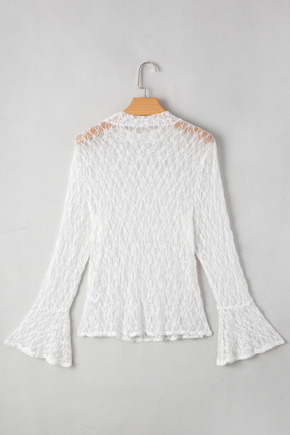 White lace blouse on a hanger against a gray background