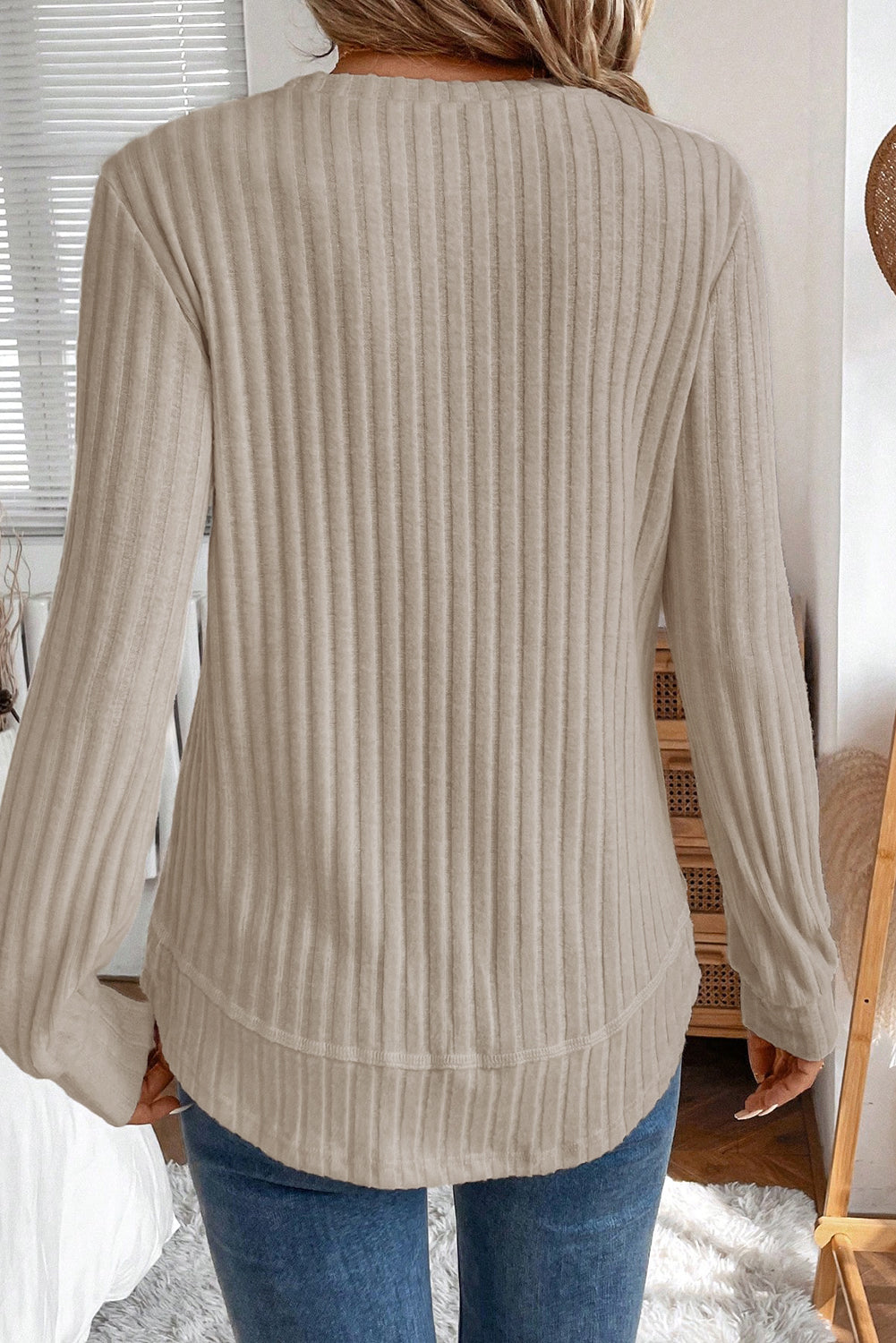 Person wearing a beige ribbed sweater and blue jeans in a home setting.