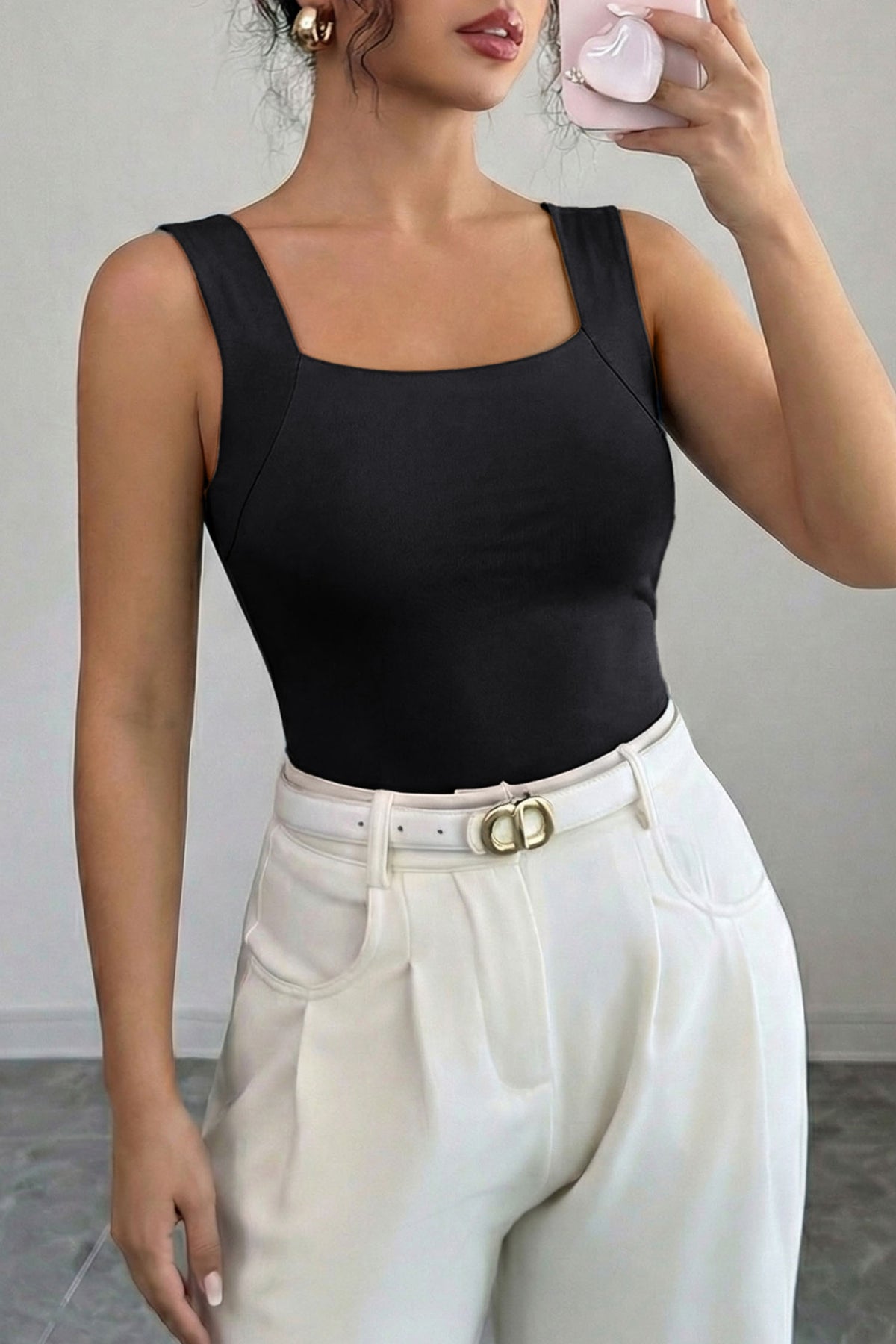 Person wearing a black tank top and white pants with a gray background