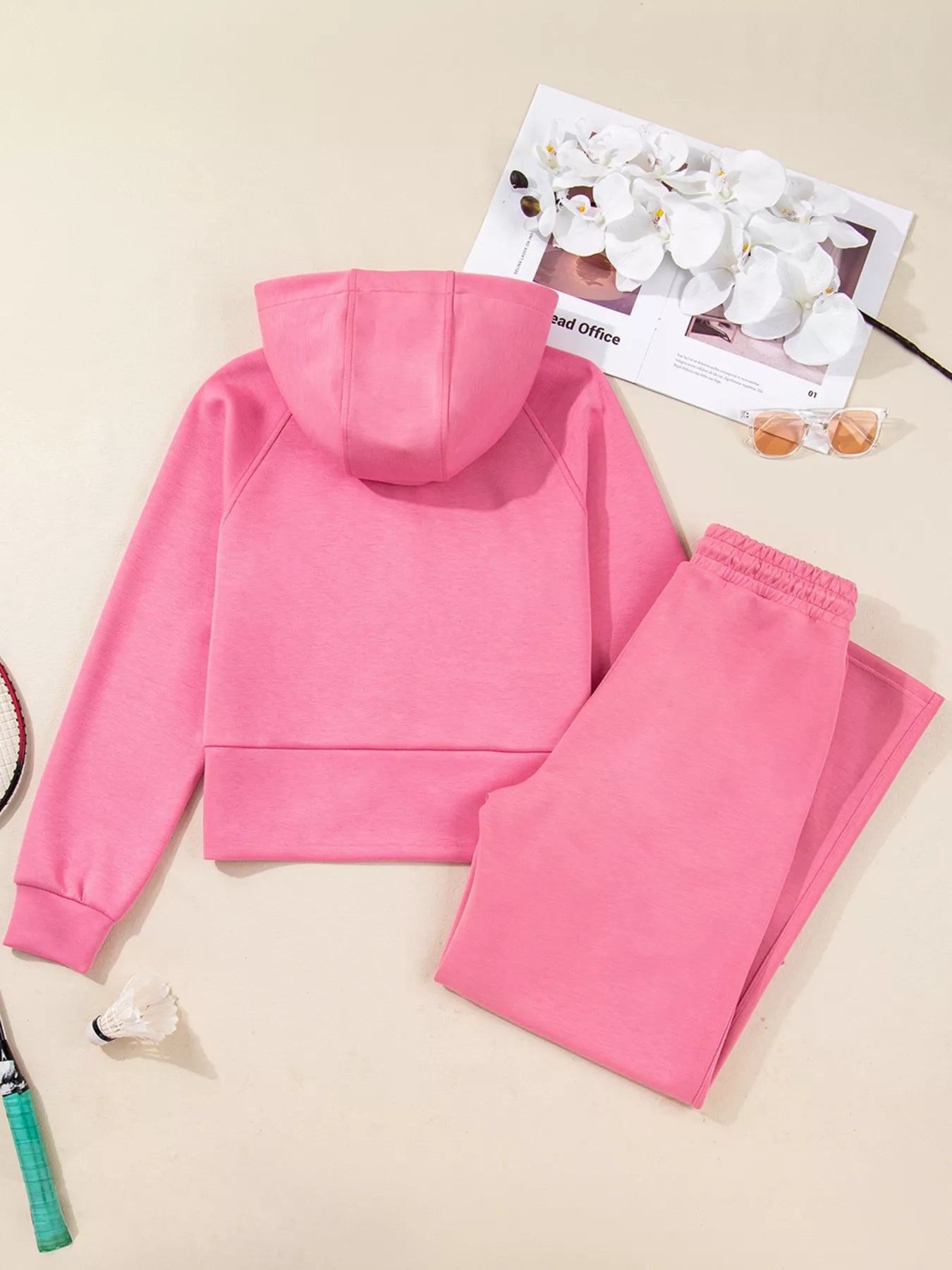 Pink hoodie and pants set on a beige surface with a magazine underneath.