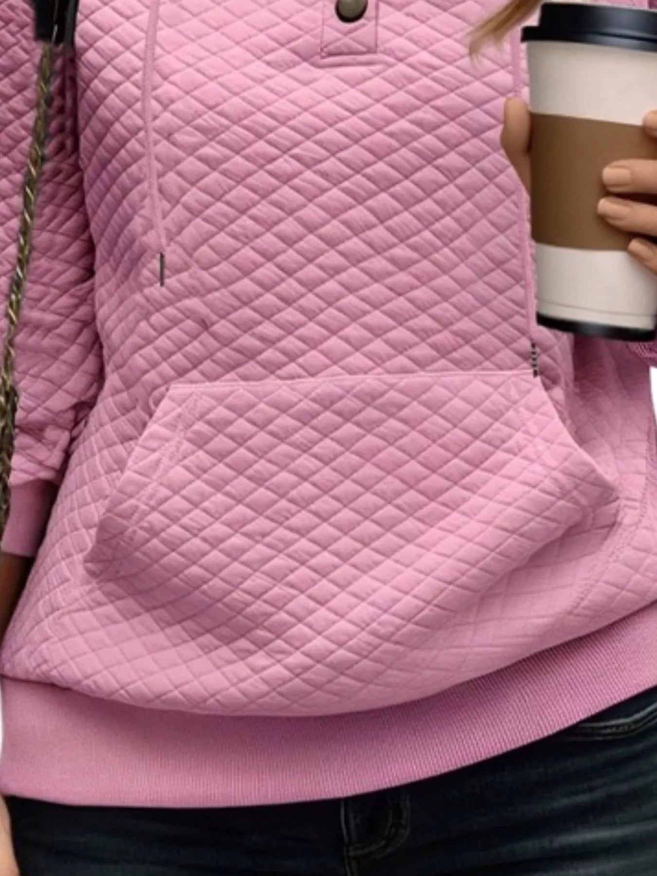 Person wearing a pink quilted jacket holding a coffee cup.