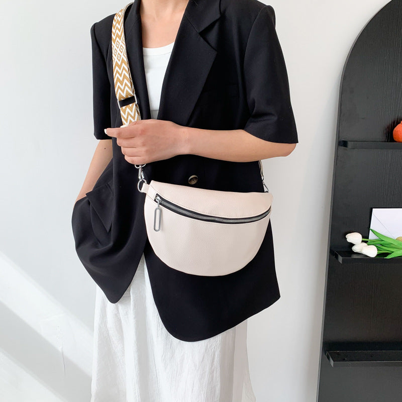 Person holding a white crossbody bag with a black jacket and white pants against a light background