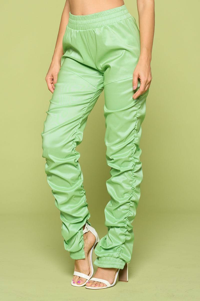 Green faux leather pants worn by a person on a green background detail view