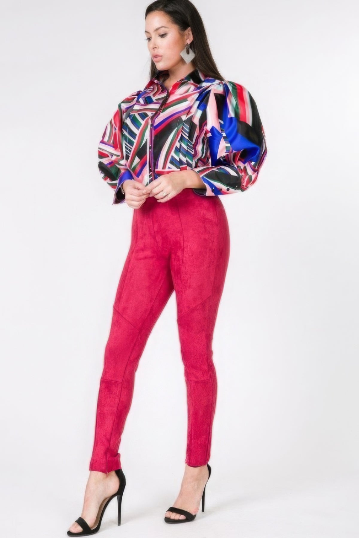 Woman wearing a colorful patterned blouse and red faux suede pants on a white background 