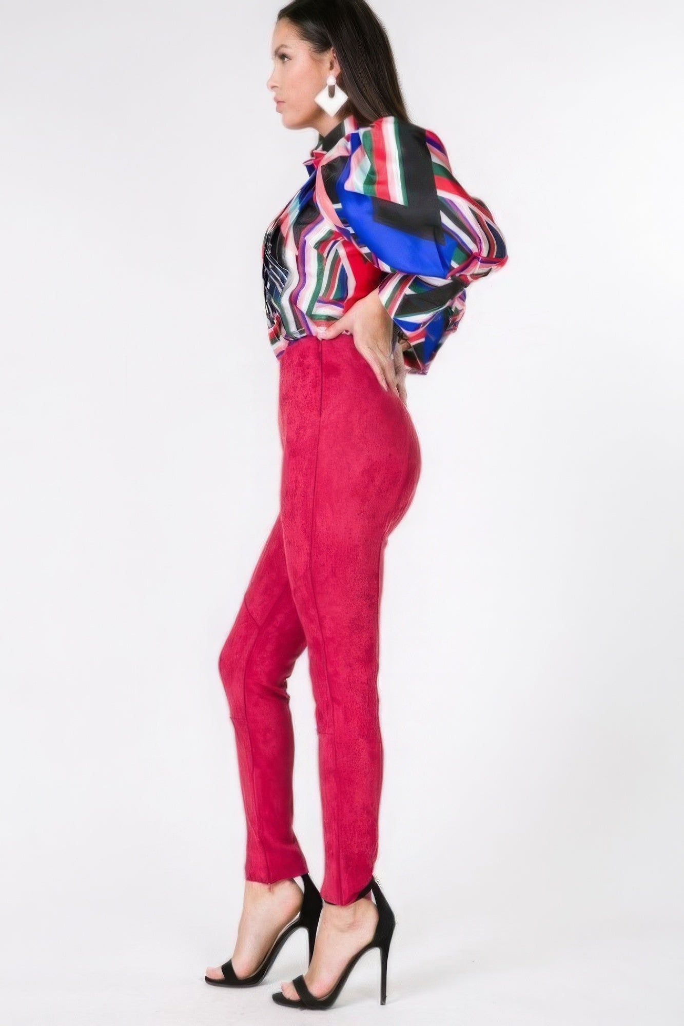Woman wearing a colorful blouse and red faux suede pants on a white background side view 