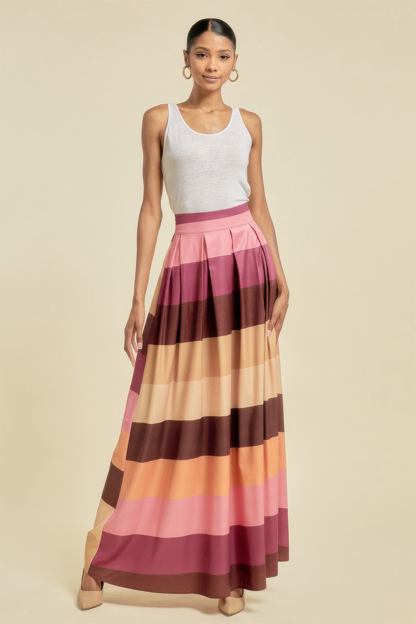 Woman wearing a white tank top and a long, multicolored striped skirt on a beige background