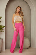 Woman wearing a white top and pink pants standing in a room with a plant and decorative ball.