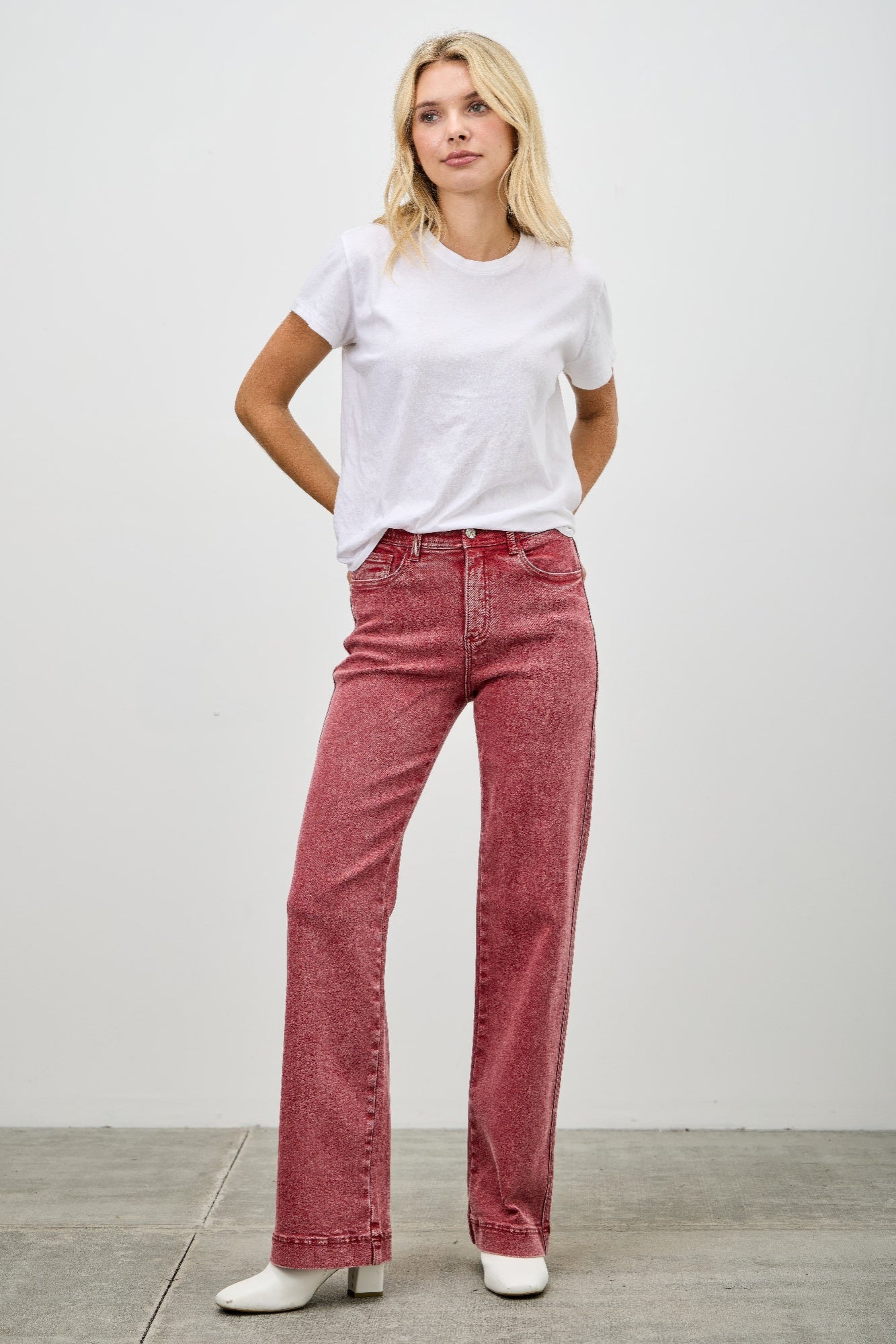 Woman wearing a white t-shirt and red jeans against a plain background
