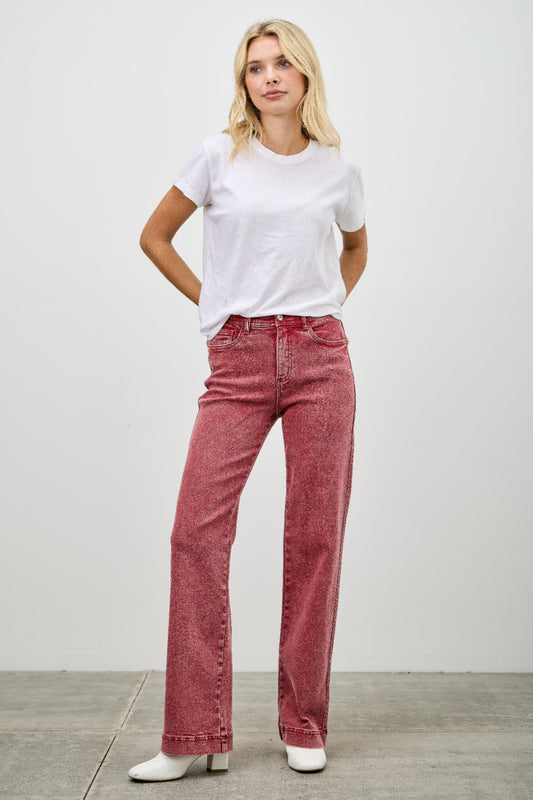 Woman wearing a white t-shirt and red jeans against a plain background