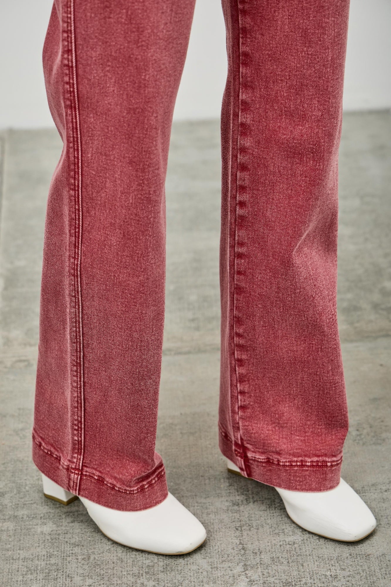 Red jeans hem view worn with white boots on a neutral background