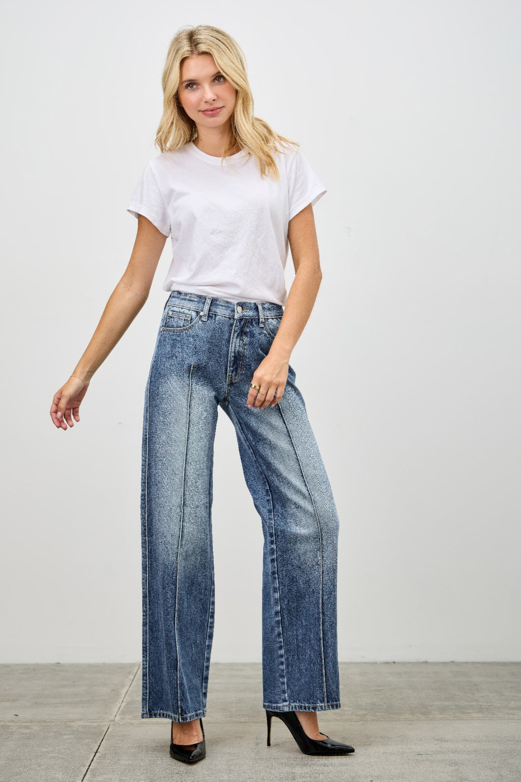 Woman wearing a white t-shirt and pintuck blue jeans against a plain background