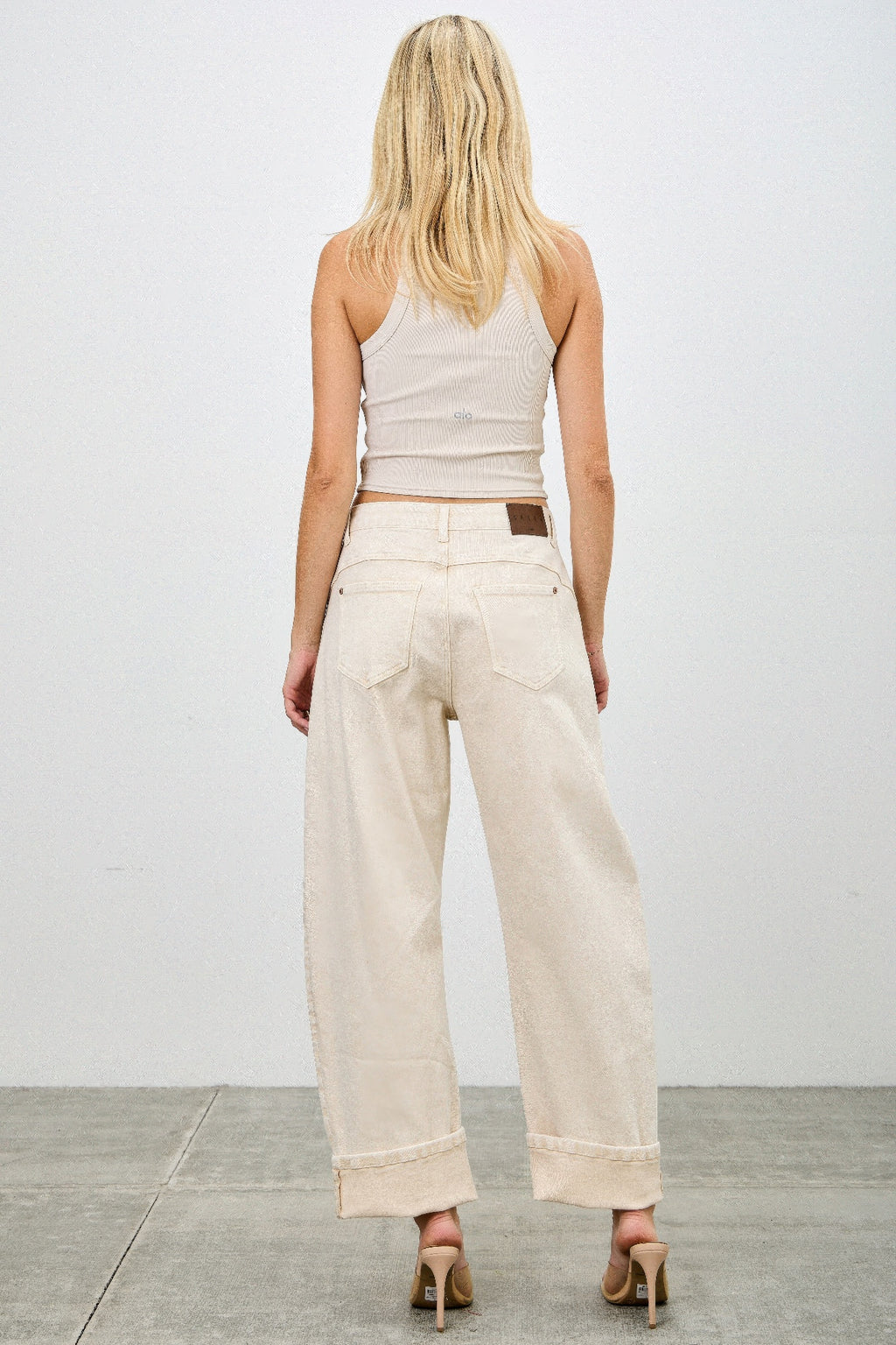 Woman wearing a white sleeveless top and beige western barrel jeans butt view